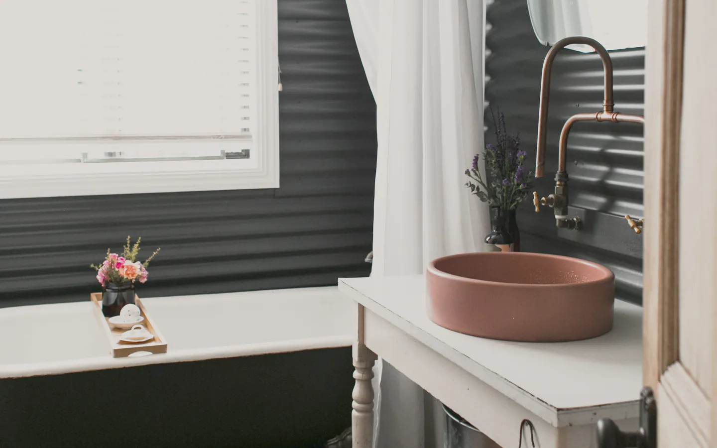 A cottage bathroom with an exposed copper shower over a clawfoot bath