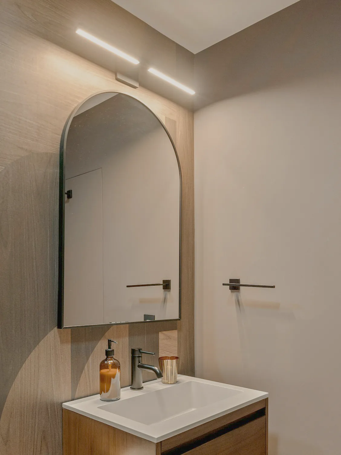 A wall hung basin under an arched mirror