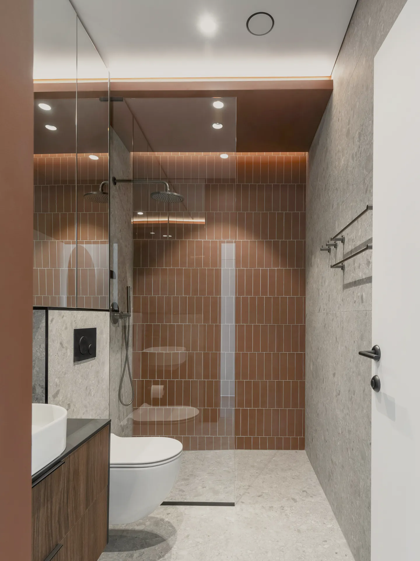 A brown tiled shower beside a dark timber vanity