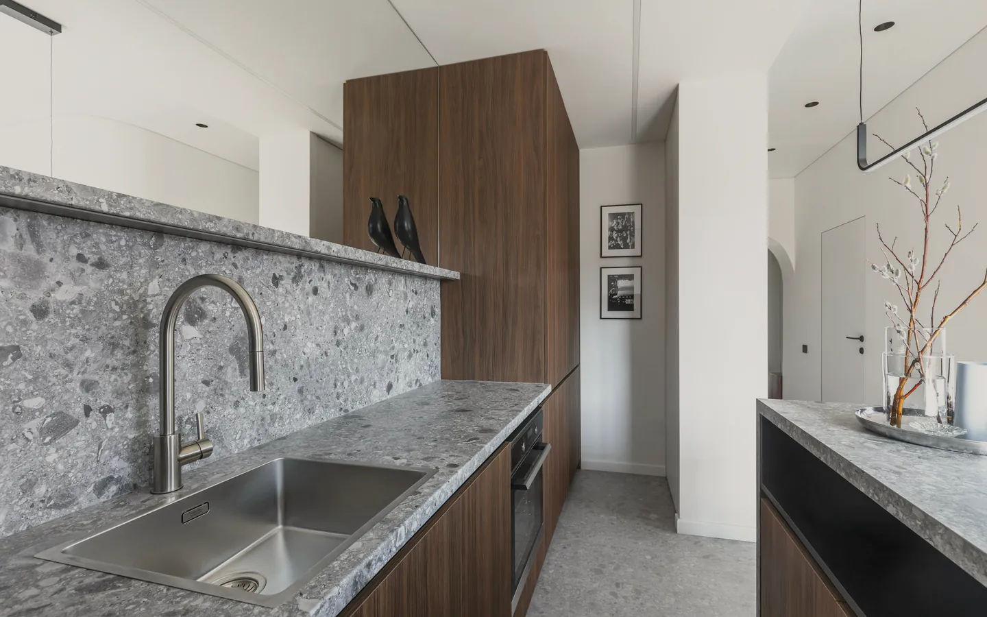 A kitchen with speckled terrazzo benches, walnut cabinets and a sink