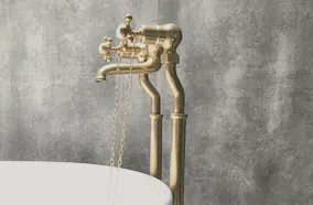A brass bath filler beside a black freestanding bath