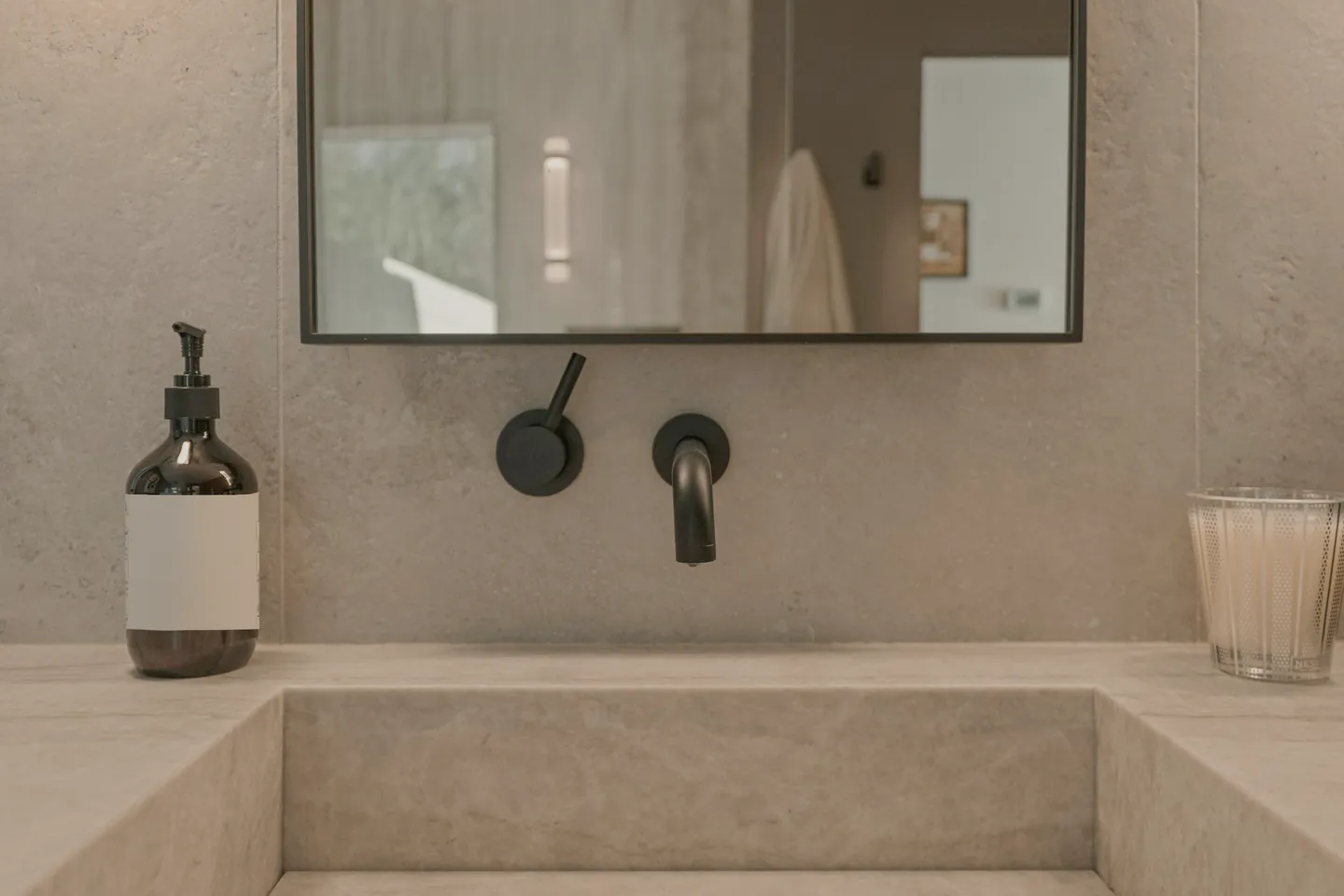 A stone trough basin with a black wall mixer under a mirror