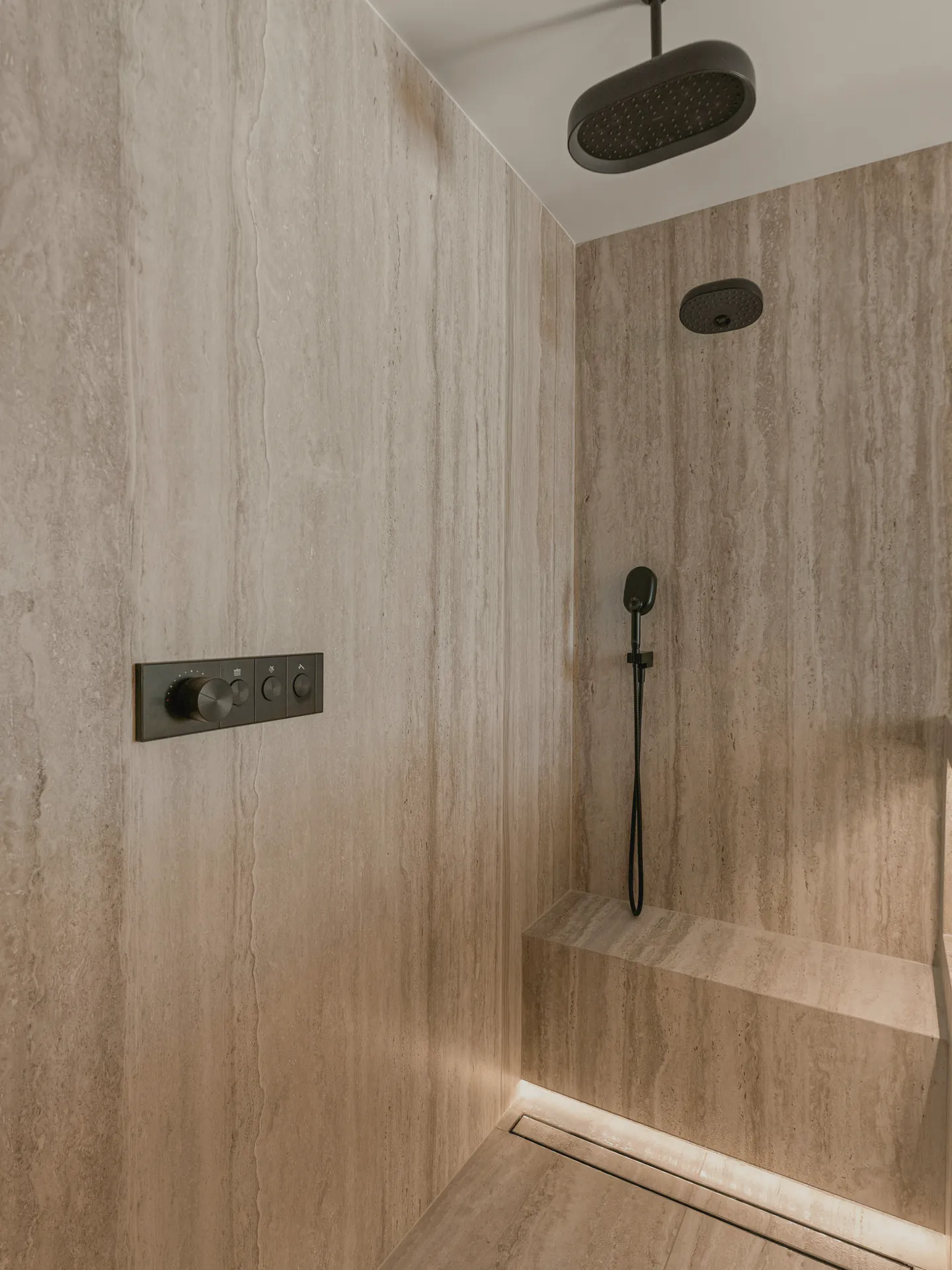 The shower bench and its lit linear drain in travertine
