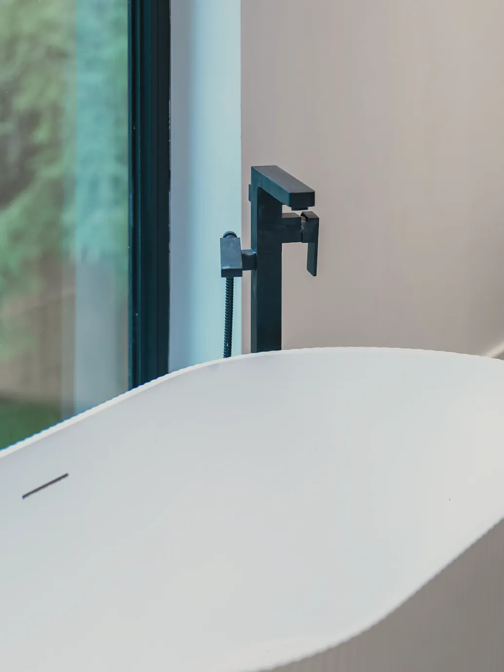 A black floor mixer beside the bath at the window